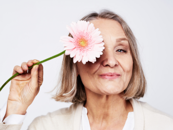 older woman holding a daisy over her right eye