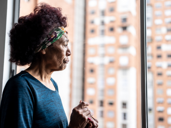 woman with concerned face looks out a window