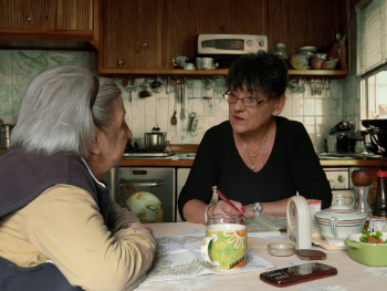 two women discuss calendar in a dated kitchen