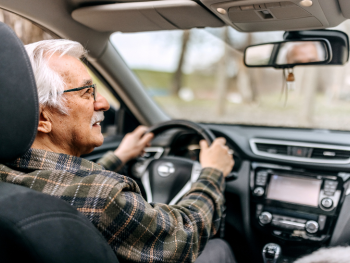 older man holding steering wheel