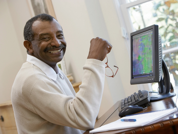 smiling man sits at desk with computer