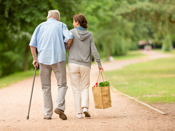 older man with cane walks arm in arm with woman